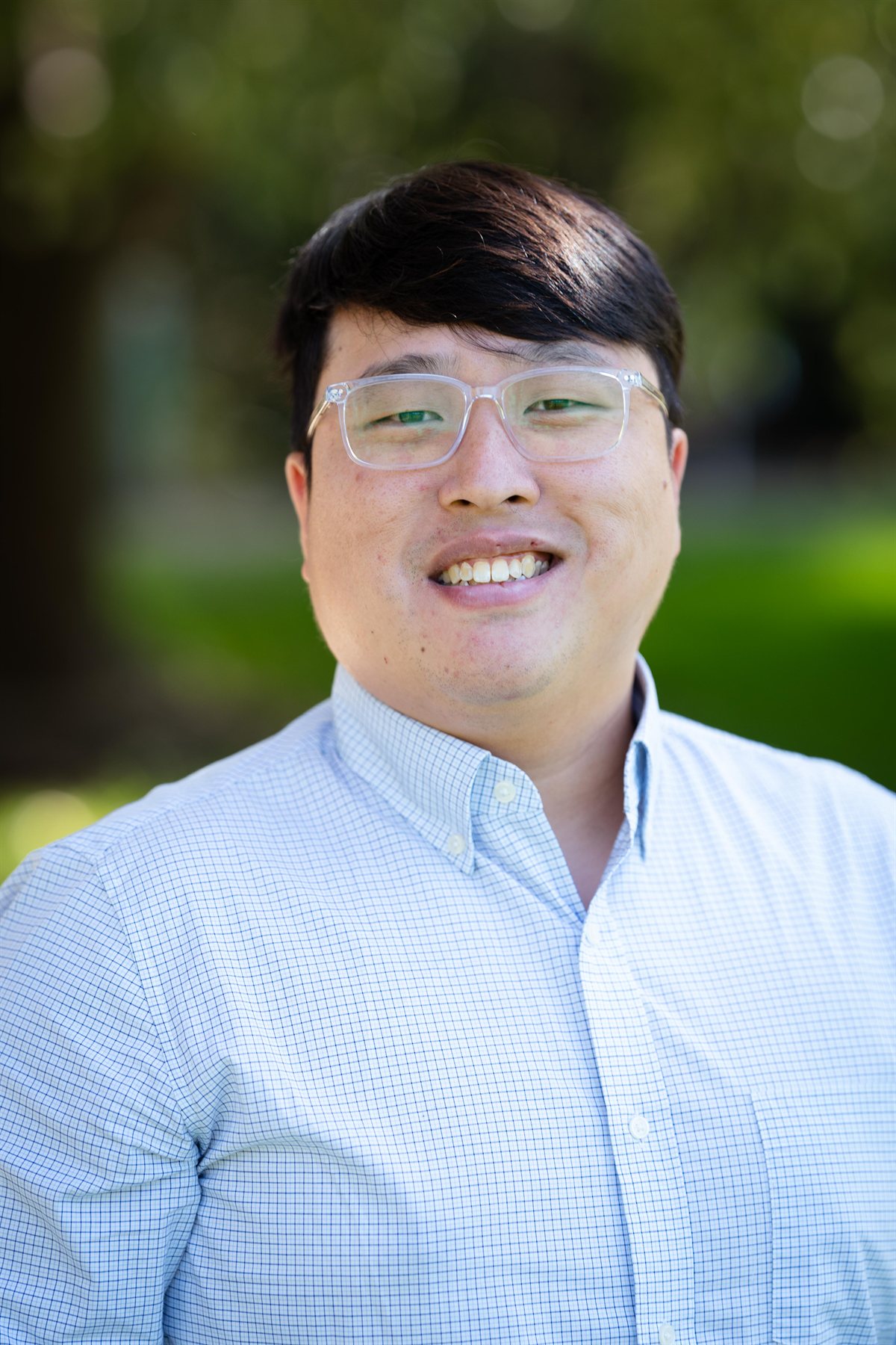 Nevin Vu smiling outdoors, wearing clear glasses and a light checked shirt